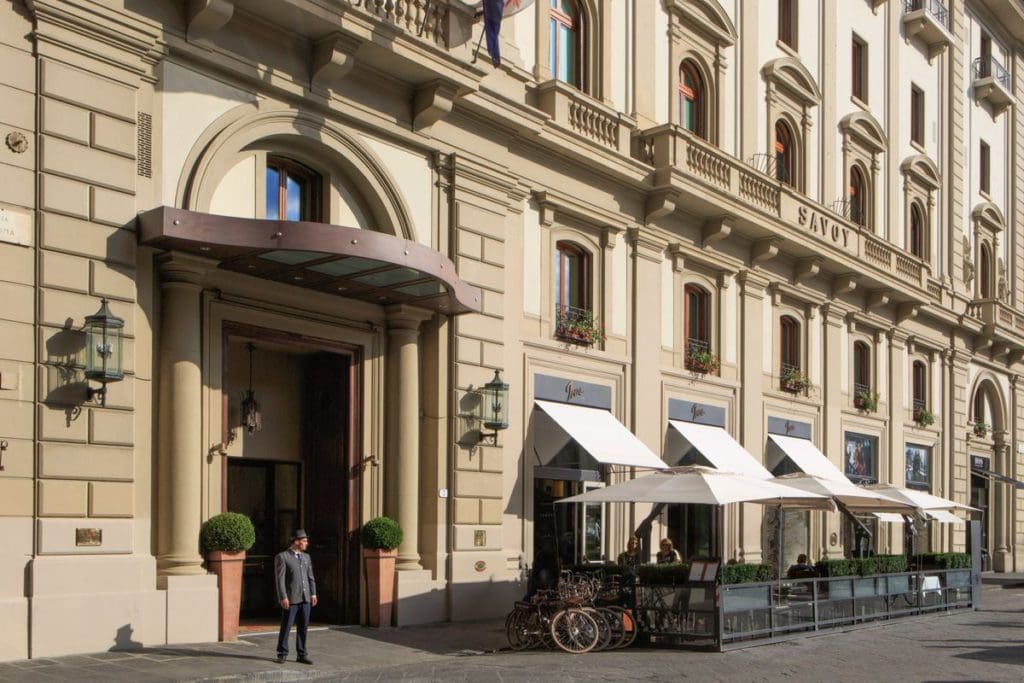 A porter walks near the entrance to Hotel Savoy in Florence on a sunny day.