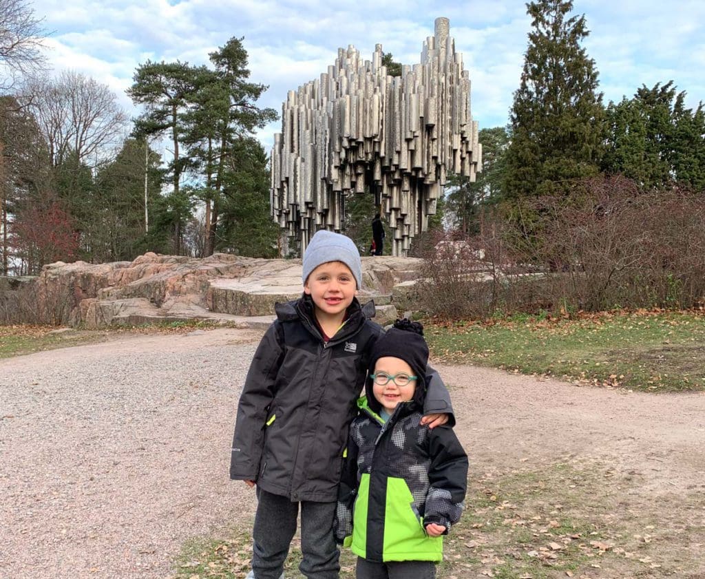 Two young boys in winter jackets stand in front of the Sebelius Monument.