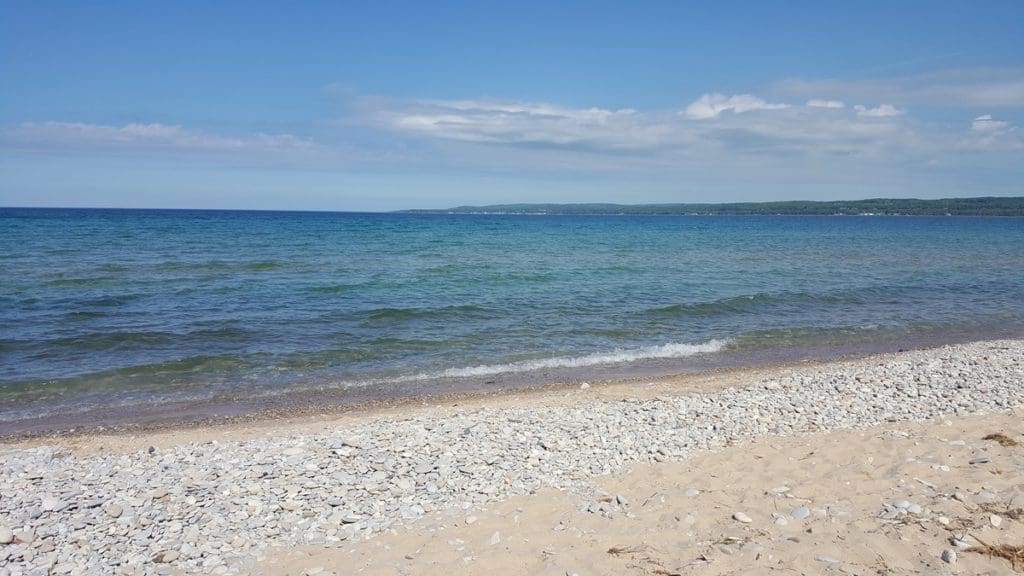 A stretch of sandy, rocky beach runs along a large lake at Petoskey State Park.