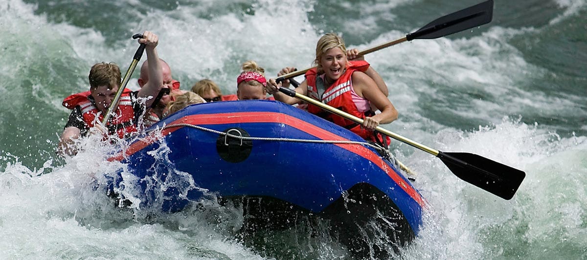 A family white water rafts down a river, while staying at Rainbow Trout Ranch, one of the best all-inclusive hotels in the United States for families.