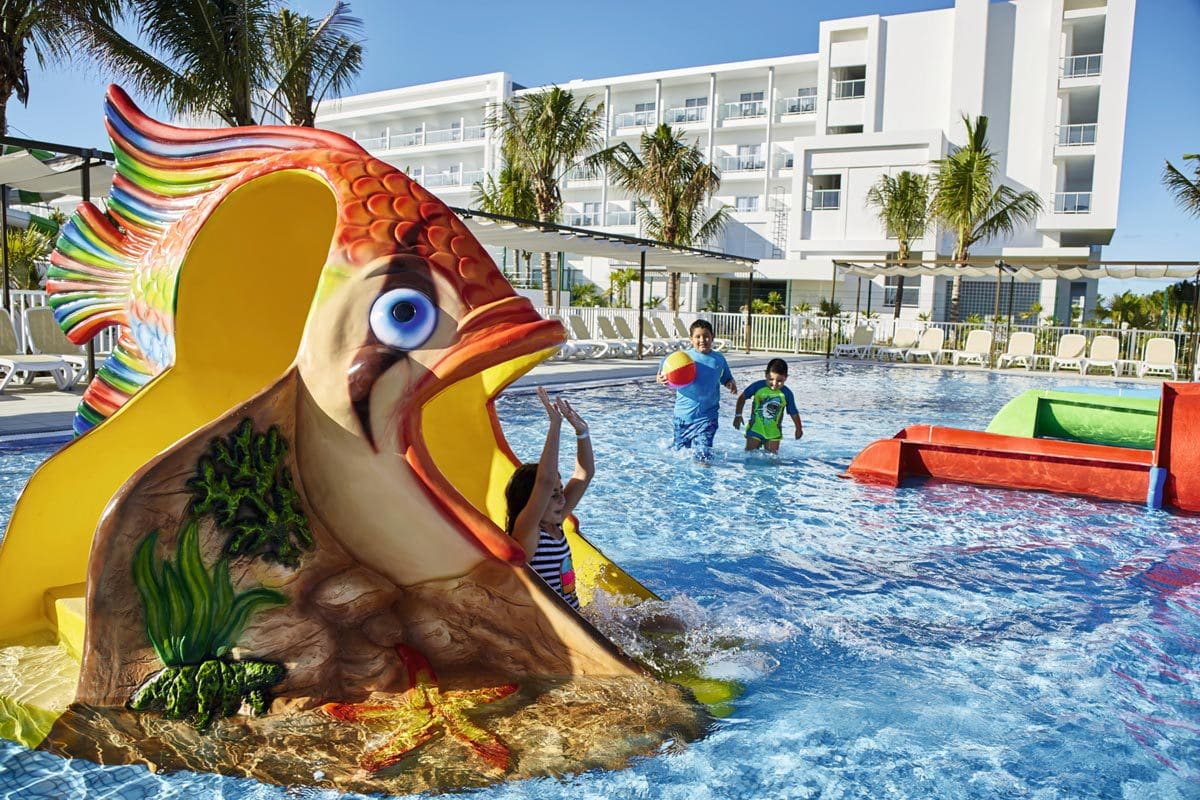 A young girl slides down a fish-shaped slide at Riu Dunamar, one of the best resorts in Mexico with a water park for families.