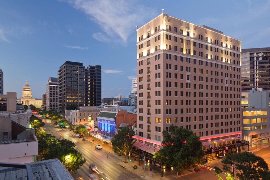 The exterior of The Stephen F Austin Royal Sonesta Hotel surrounded by other large buildings in Austin.