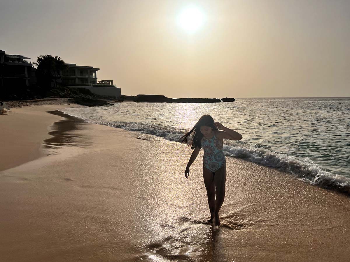 A young girl walks along the beach at sunset.