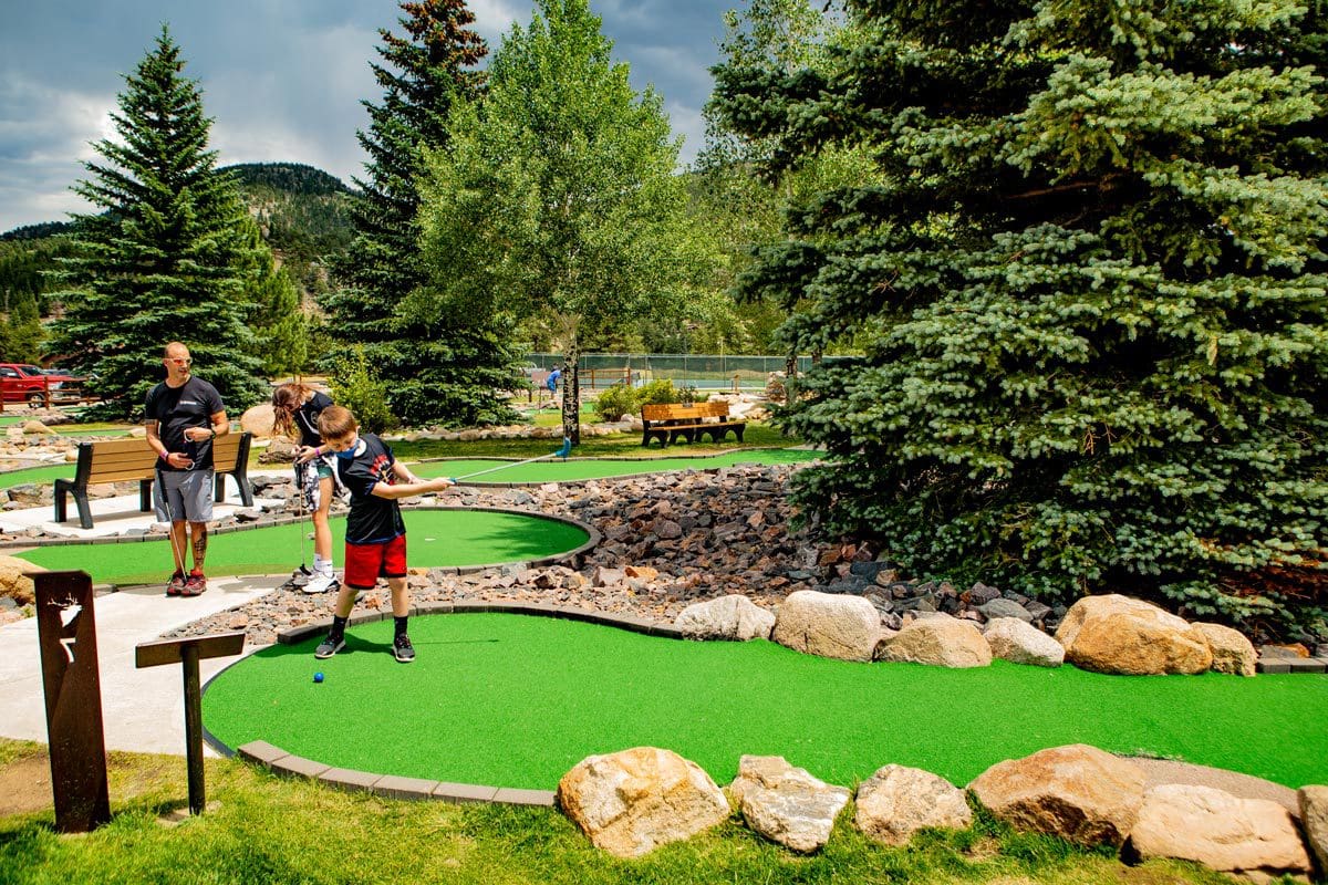 A young boy and his dad mini golf on a sunny day, while staying at YMCA of the Rockies.