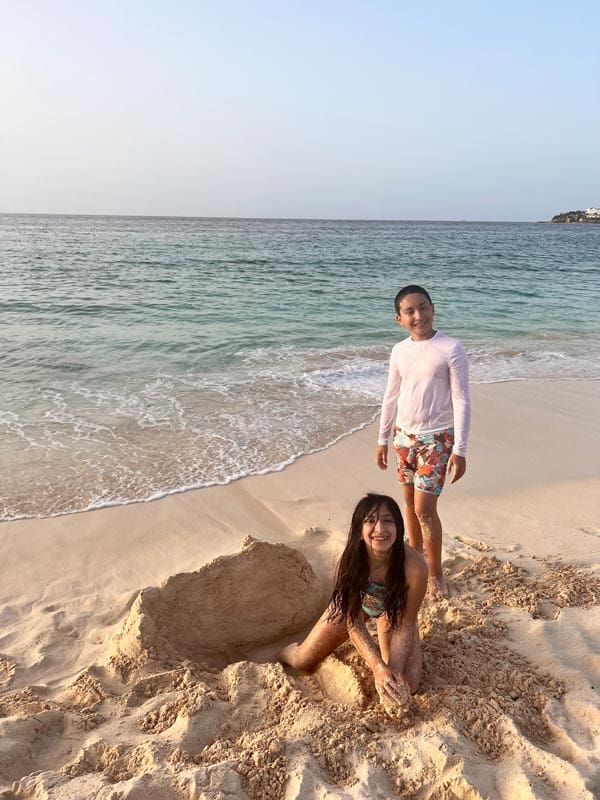 Two kids dig in the sand along the ocean on a sunny day.
