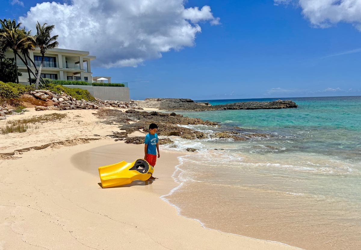 A young boy pulls a glass boat along the sand toward the ocean in Anguilla on a sunny day.