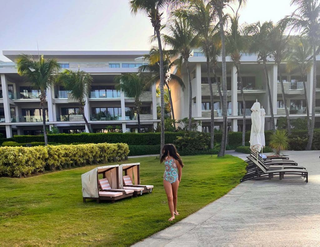 A young girl wearing a swimsuit walking along the sidewalk, between empty chairs, at Four Seasons Resort and Residences Anguilla.