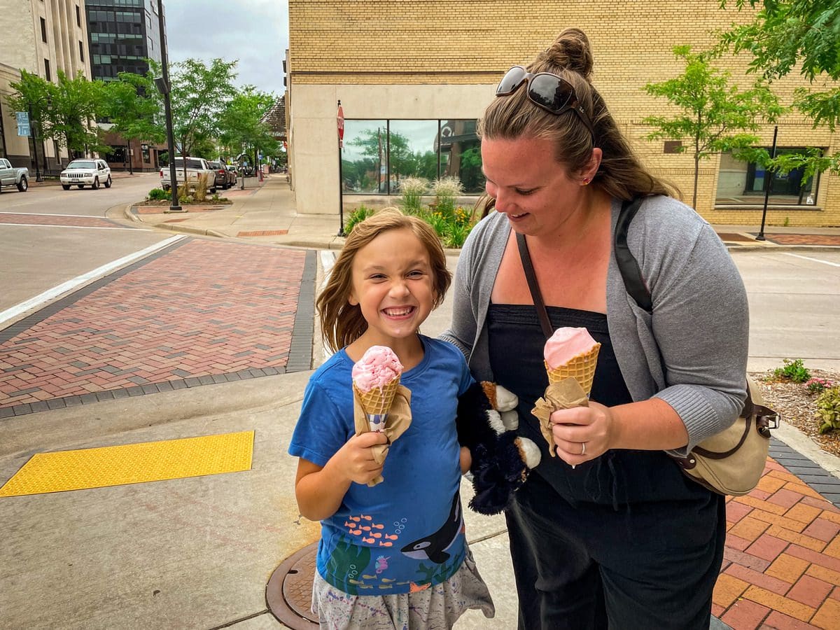 A mom and her young daughter stand on a downtown street corner, smiling as the hold two huge ice cream cones from Olson's Ice Cream.