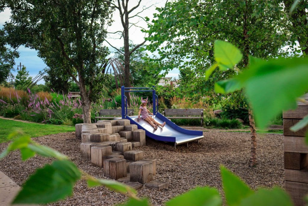 A young girl slides down a metal slide on a playground at River Prairie Park, one of the best things to do in Eau Claire with kids.