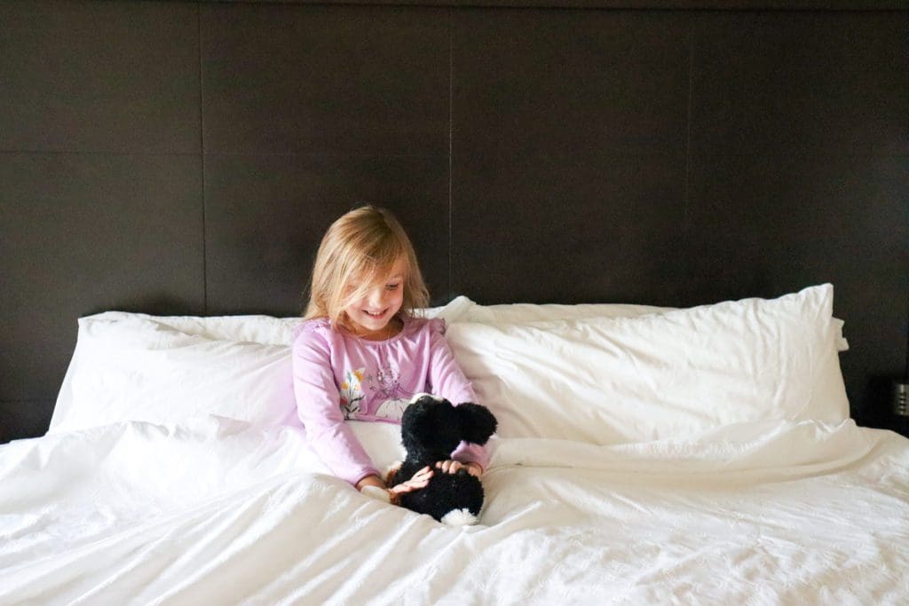 A young girl is tucked into bed with her stuffie at the Staybridge Suites Eau Claire - Altoona.