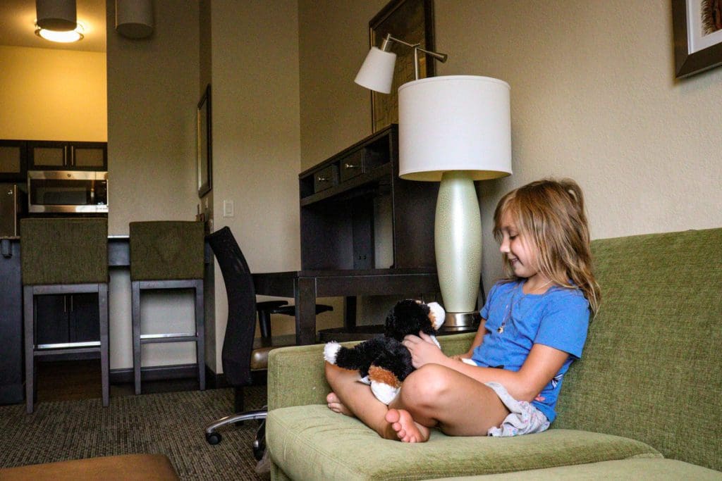 A young girl sits on a hotel couch with her stuffie, while exploring Eau Claire with her family.