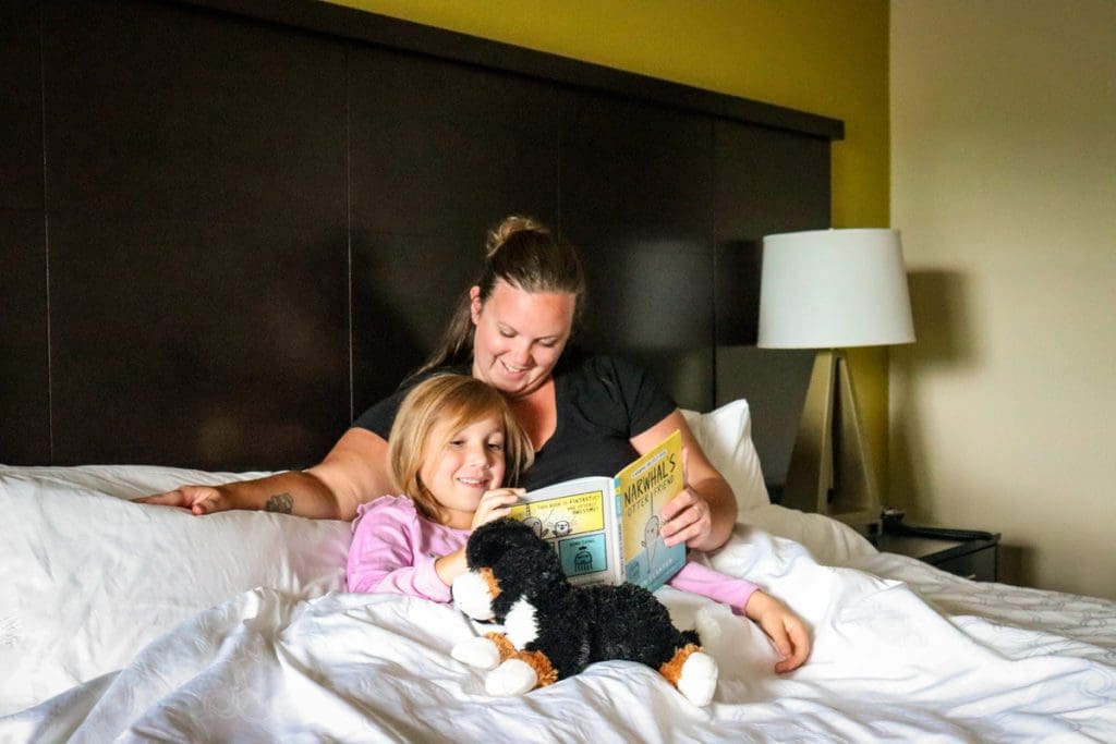 A mom and her young daughter read a book together, while snuggled up in bed at the Staybridge Suites in Eau Claire.