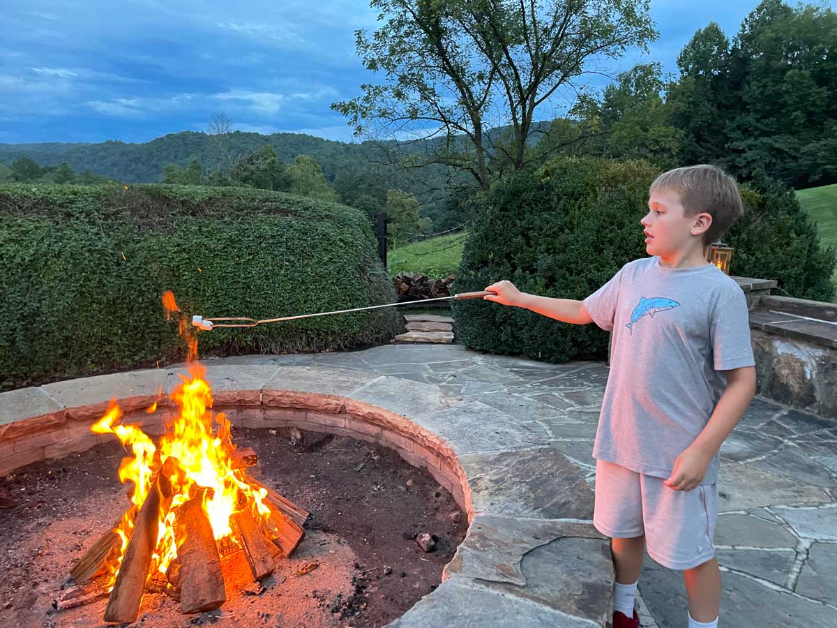 A young boy roasts a marshmallow over a bonfire pit, while on a family getaway to Blackberry Farm in Tennessee..