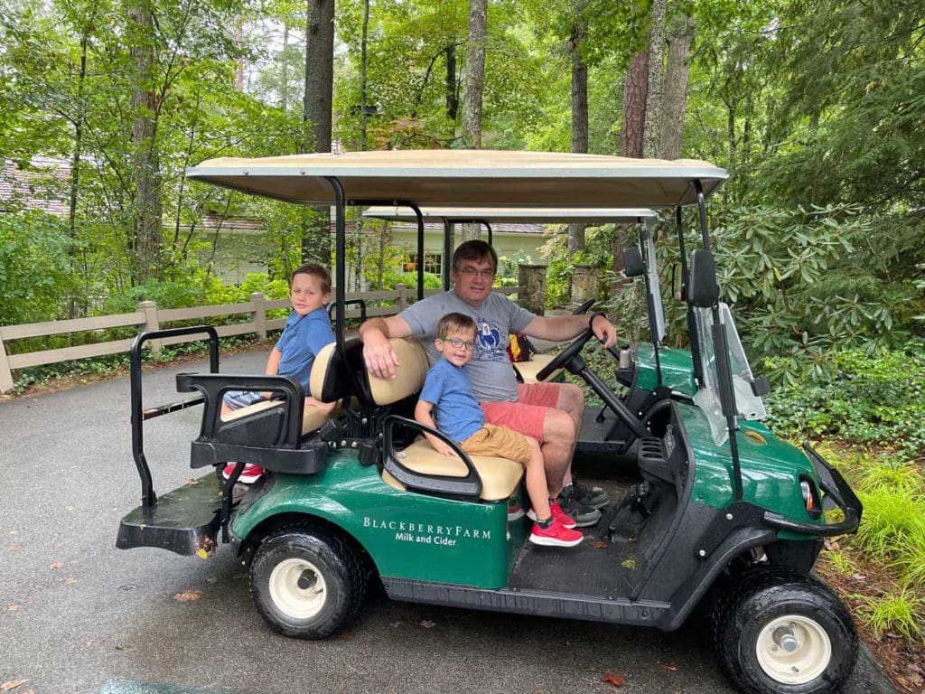 A dad and his tow young sons sit in a parked golf cart, while on a family getaway to Blackberry Farm in Tennessee.