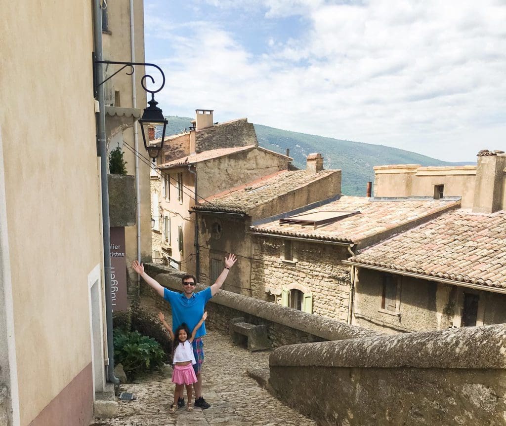 A young girl and her dad stand together with a rooftop view of Bonnieux behind them.