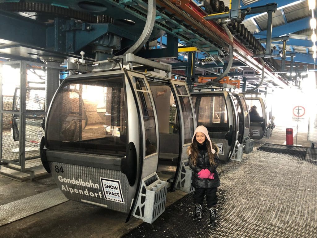A young girl stands near the entrance to a gondola in Alpendorf, ready to ski for the day.