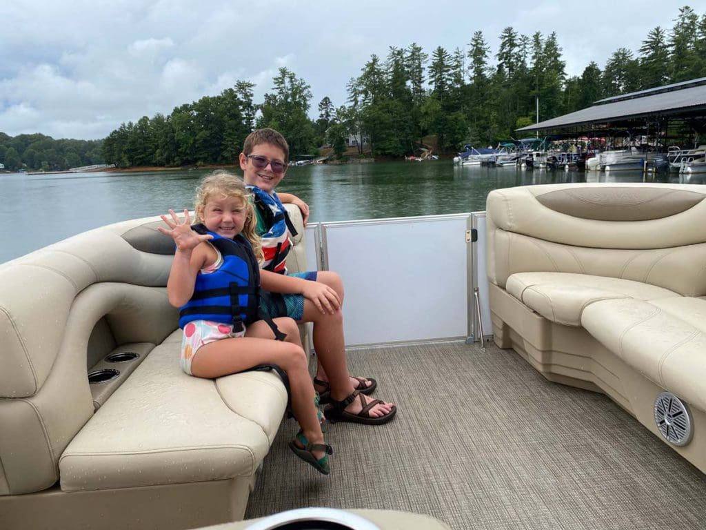 Two kids sit smiling in a pontoon sailing across Blue Ridge Lake, one of the best family activities in North Georgia Mountains.