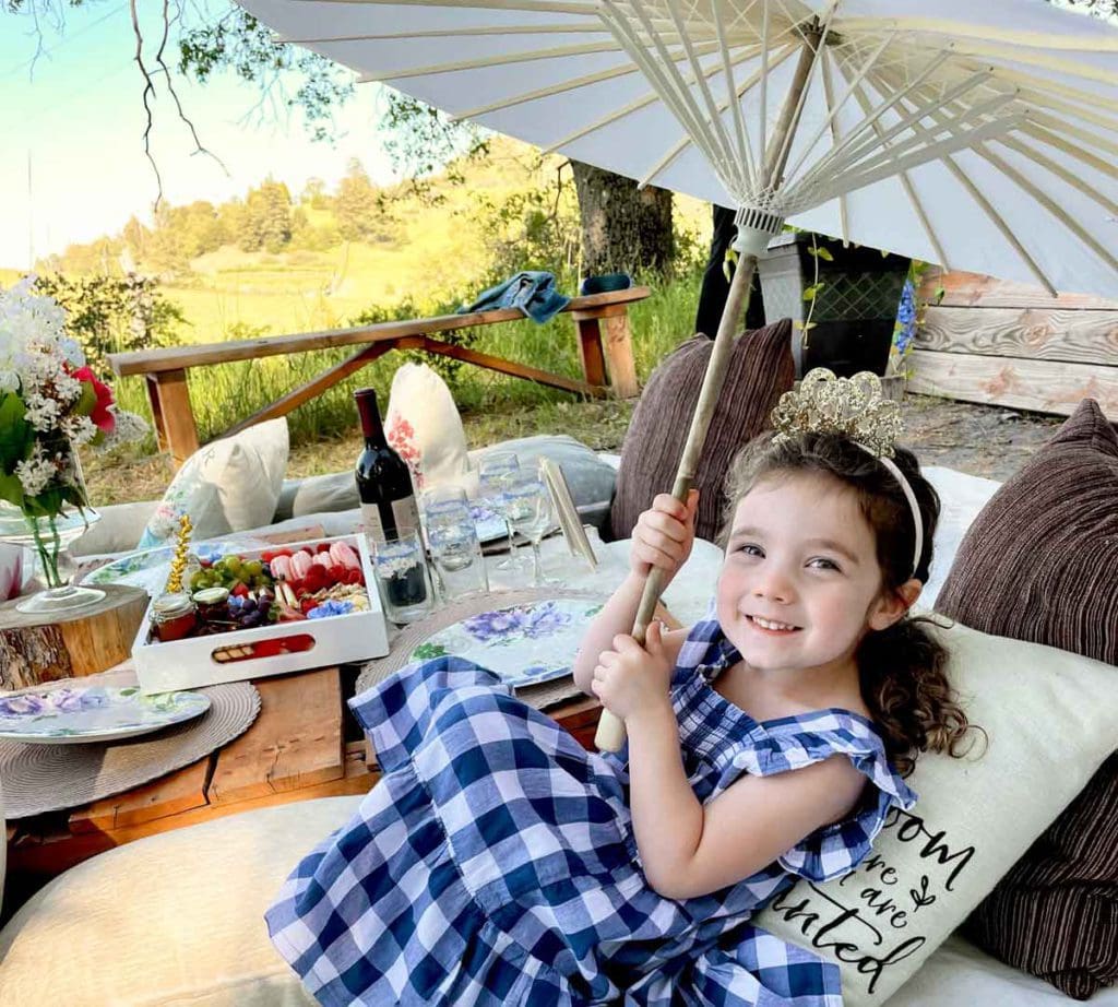 A young girl sits on a porch holding a parasol, while visiting a family-friendly winery, one of the best places to visit in Julian with kids.