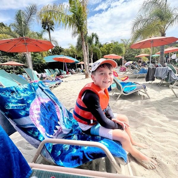 A young boy lounges on a poolside beach chair on a sunny day.
