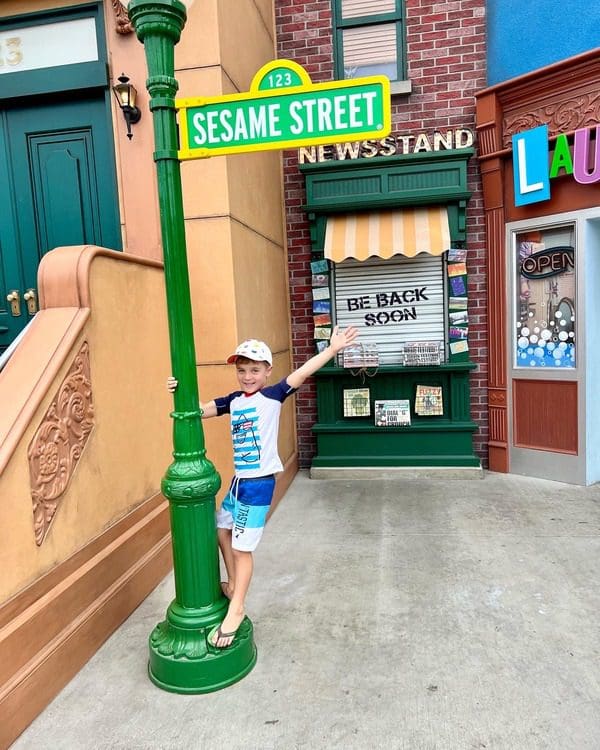 A young boy leans from the Sesame Street sign.