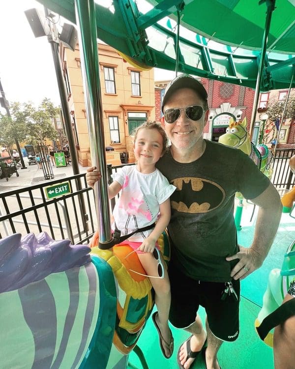 A dad stands beside her daughter, who sits atop a carousel horse.