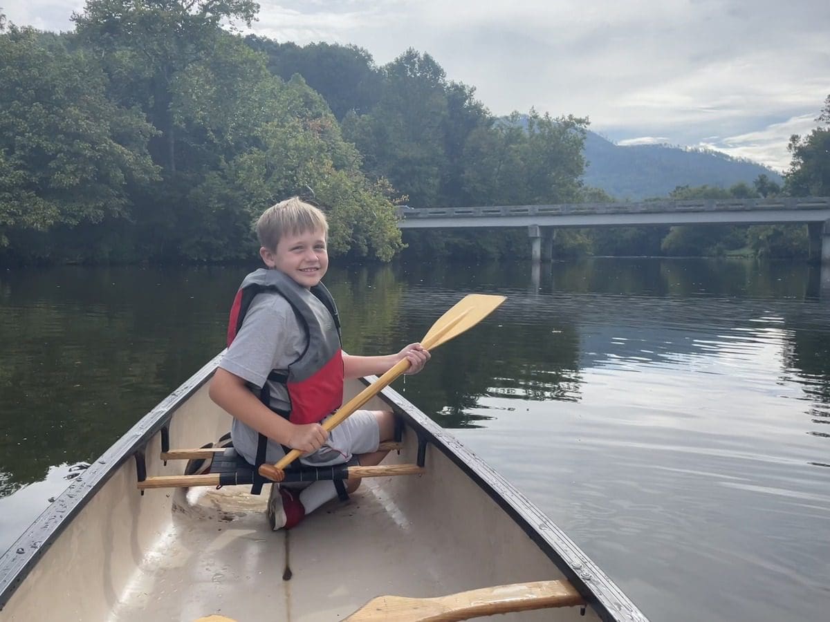 A young boy paddles a canoe while exploring the river near Blackberry Farm.