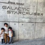 Three young boys stand at the entrance sign for Star Wars Galactic Starcruiser.
