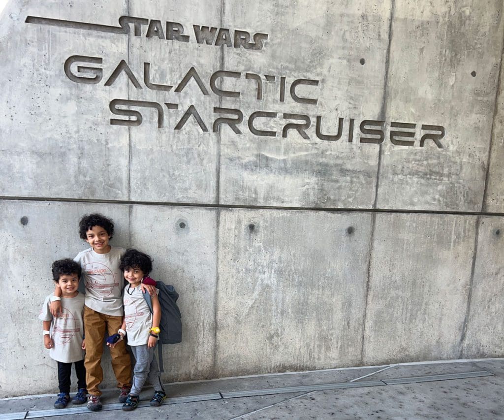 Three young boys stand at the entrance sign for Star Wars Galactic Starcruiser.