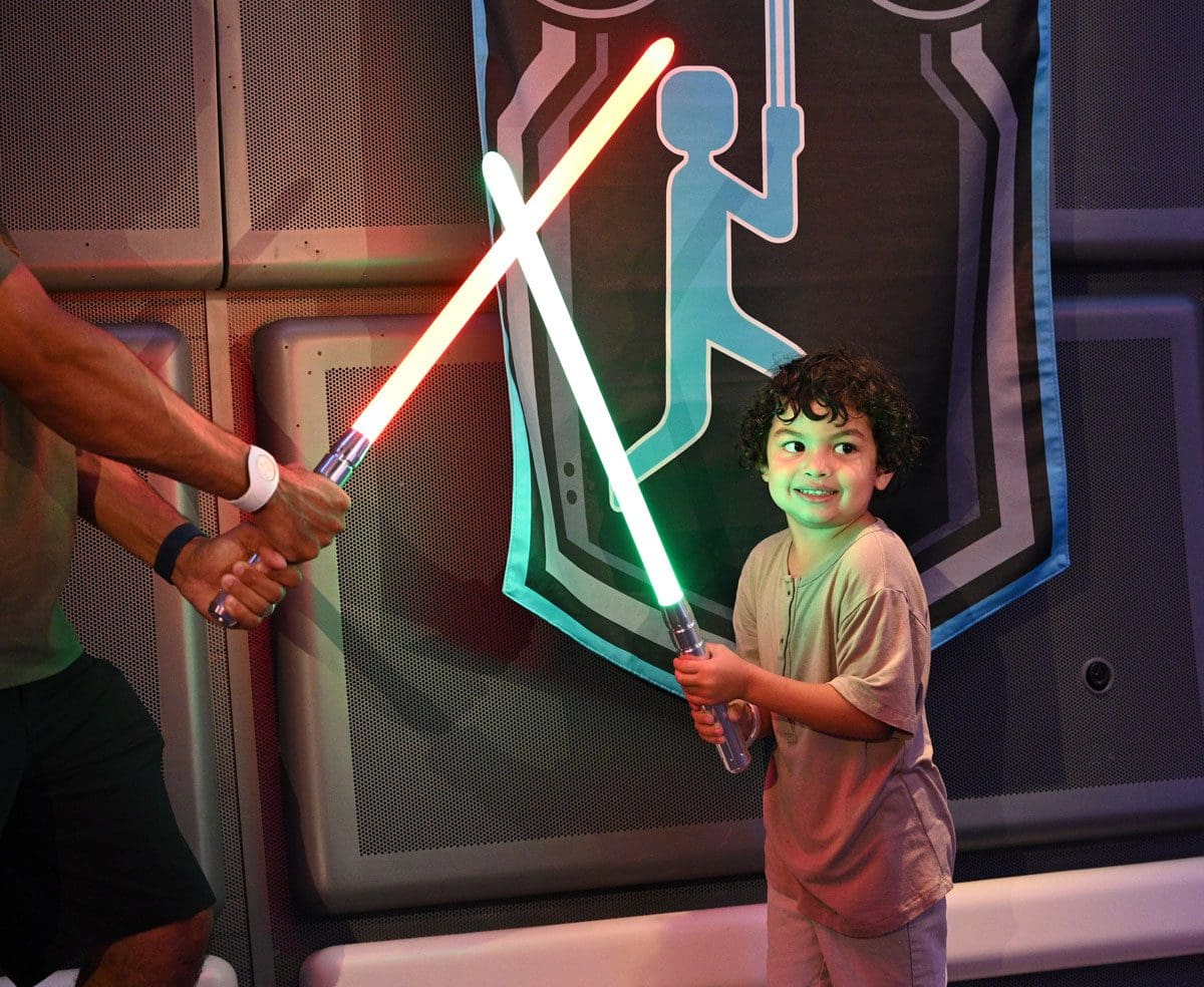 A young boy swings his light saber, while in costume on the Star Wars Galactic Starcruiser.