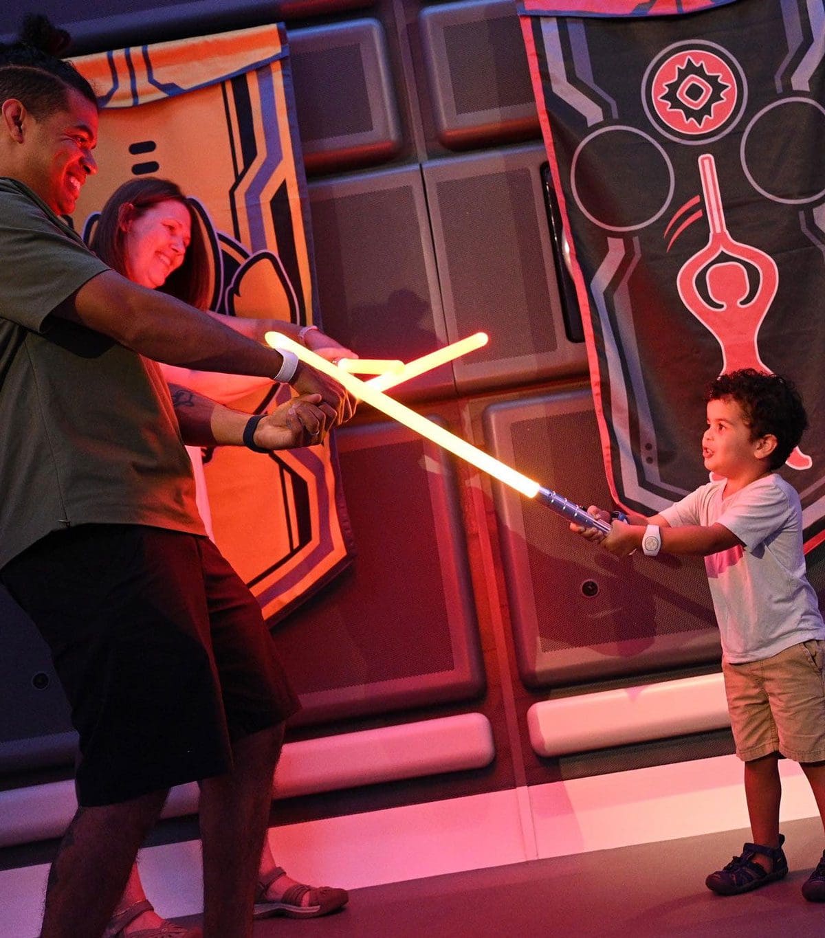 Parents and their young son pretend to battle with light sabers.
