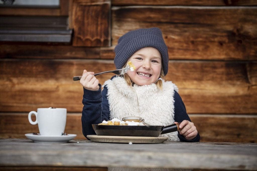 A young girl eats an alpine-inspired meal in St. Johann in Salzburg, where to eat is an important part of this family skiing in Alpendorf itinerary.