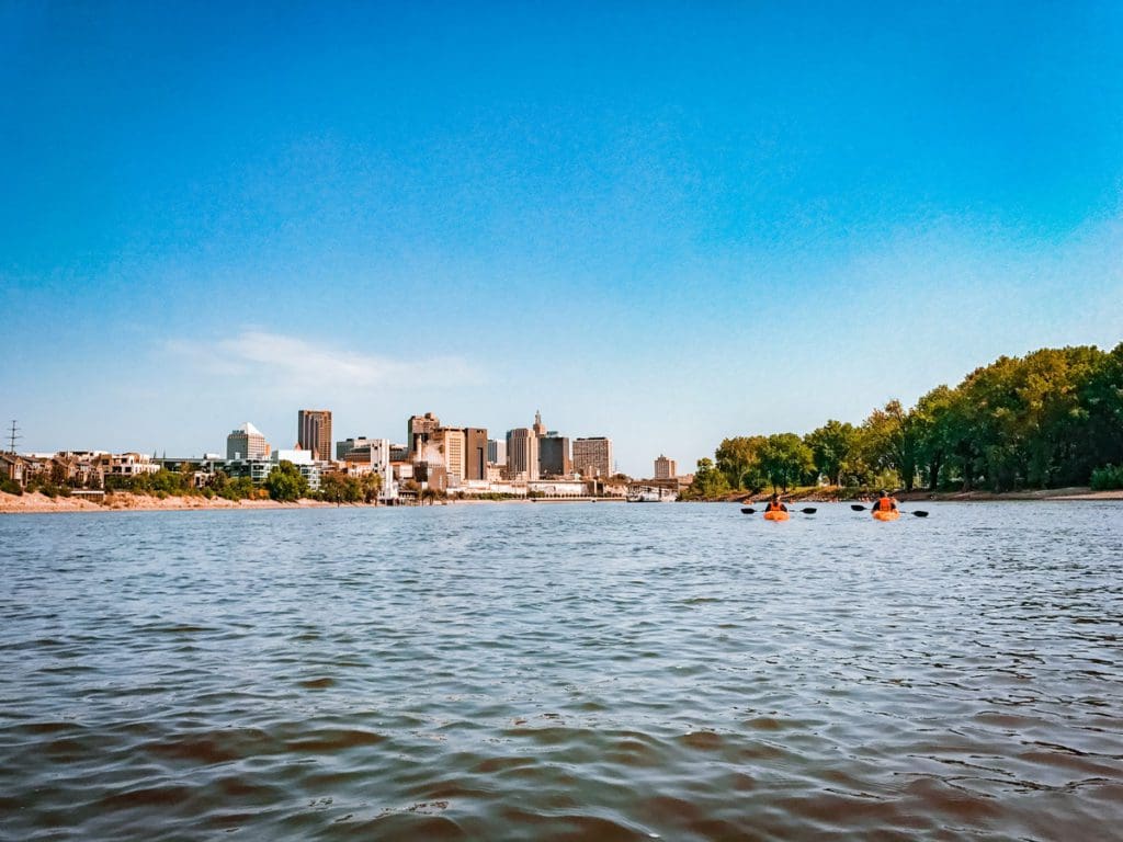 People paddle kayaks along a river with the St. Paul skyline in the distance, one of the best places to explore in the Twin Cities with kids.