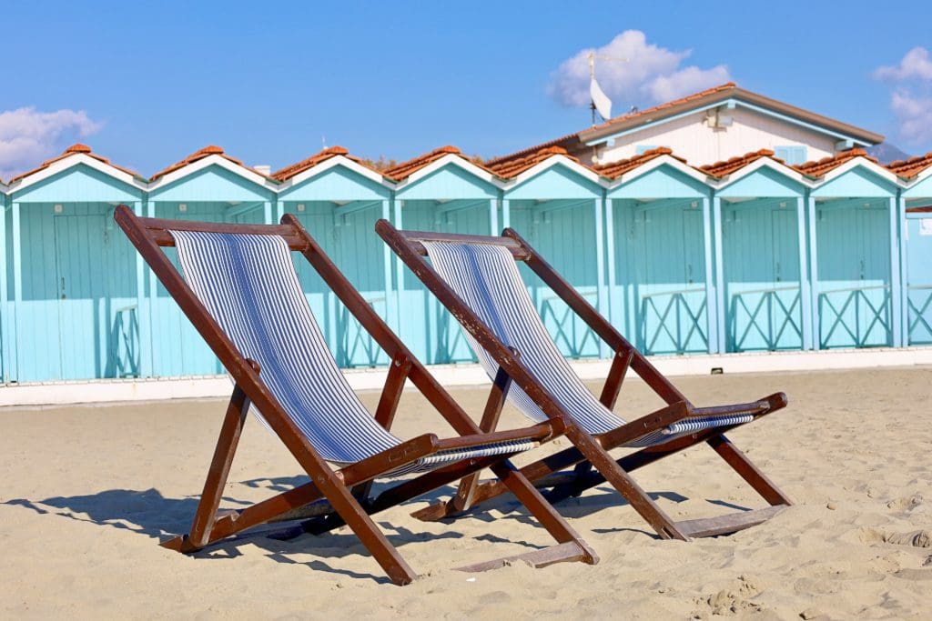 Two blue-striped beach loungers rest in the sand, with turquoise changing cabanas in the background, at Forte dei Marmi.