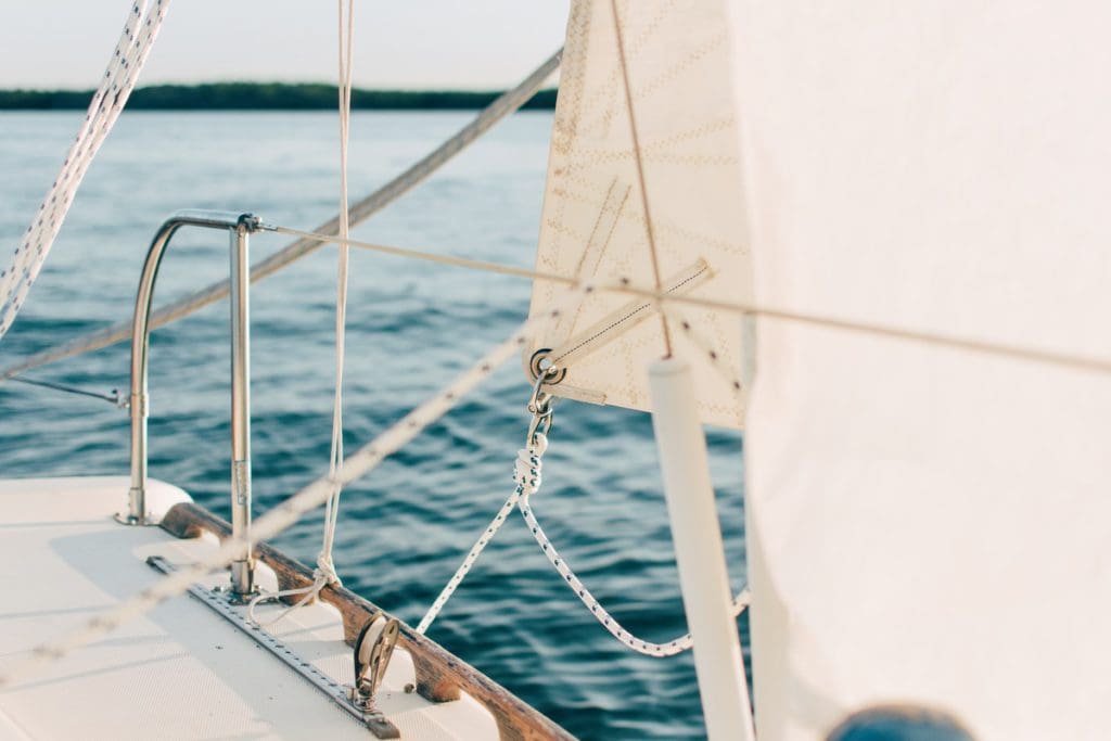 A close up of ropes and drawn sails on a sail boat in the water.