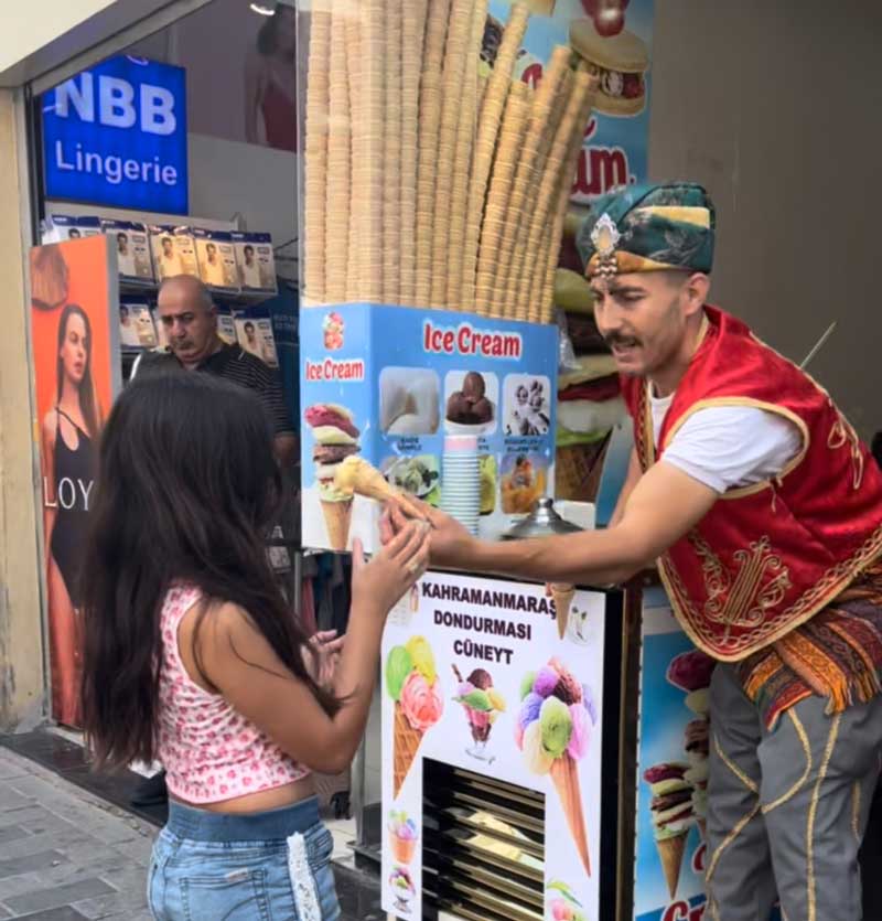 A man hands over a scooped ice cream cone to a young girl in Istanbul, knowing what to do is part of learning all about Turkey with kids.