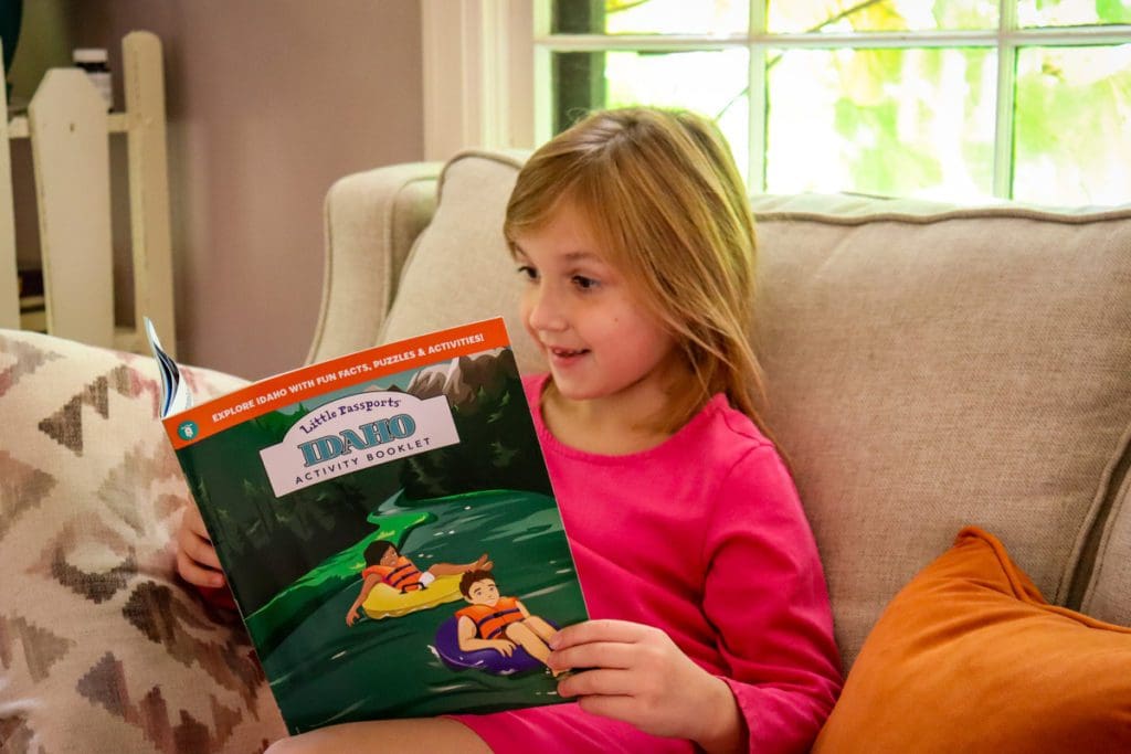 A young girl sits on the couch and reads about traveling to Idaho.