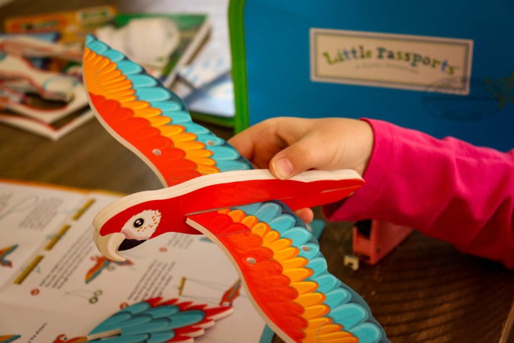 Close up of a little hand holding a macaw built from materials sent with a Little Passports subscription box.