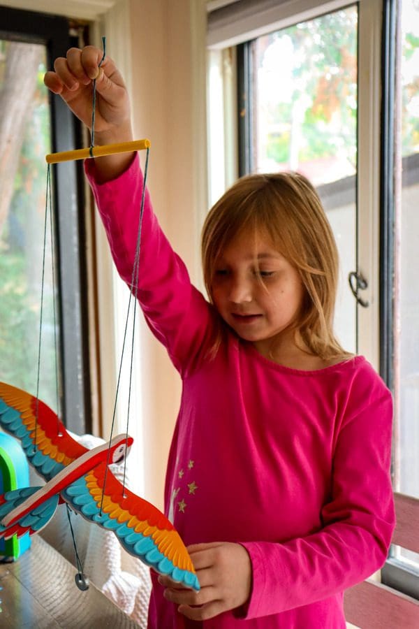 A young girl holds up her macaw activity, built on strings to pull in order to make the bird flap.
