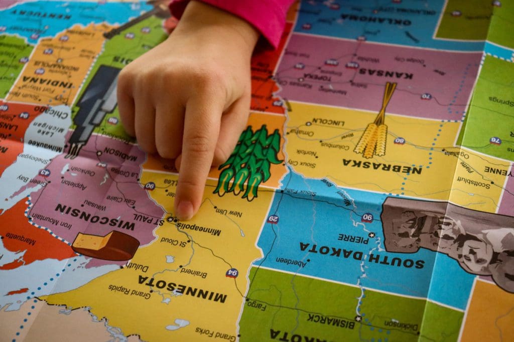 A little hand reaches out to point to Minnesota on a map of the United States.