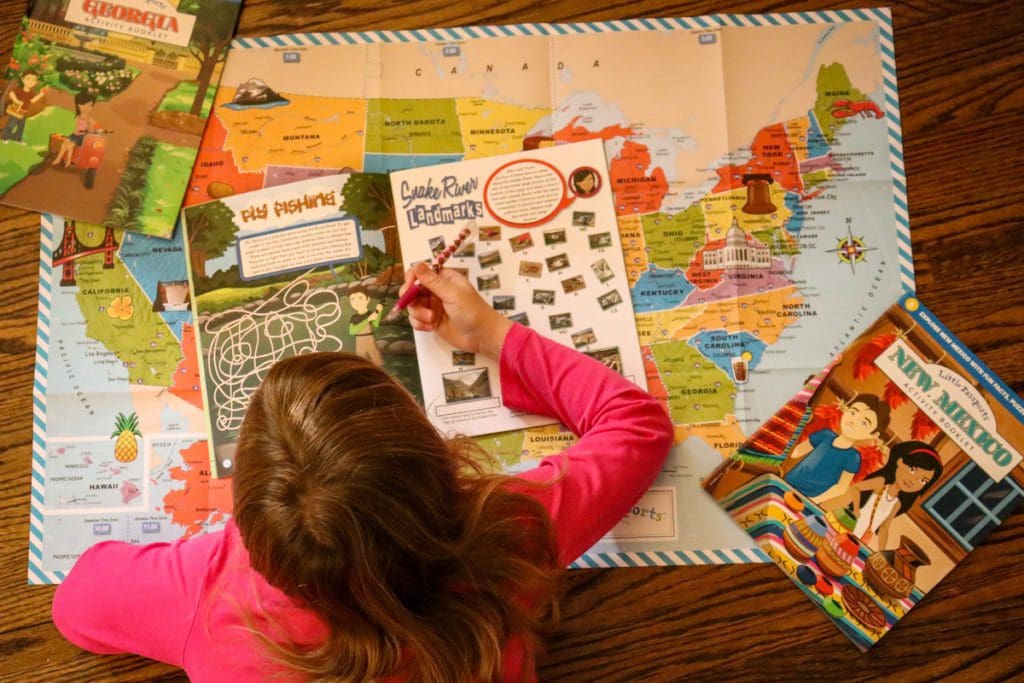 A young girl works in a Little Passports activity book, with a large map out in front of her.