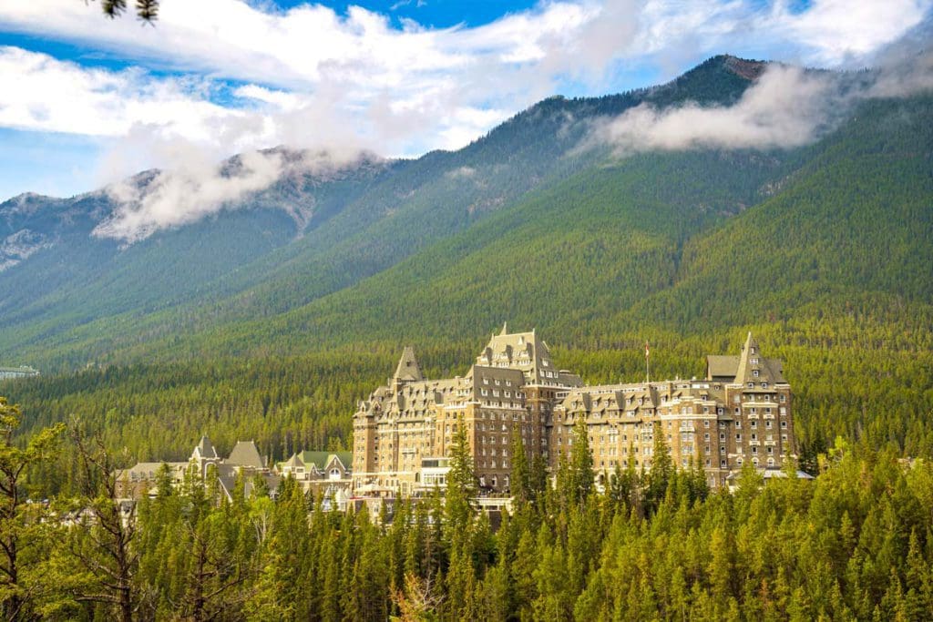 Fairmont Banff Springs Hotel rises from the pines with mountains in the distance.