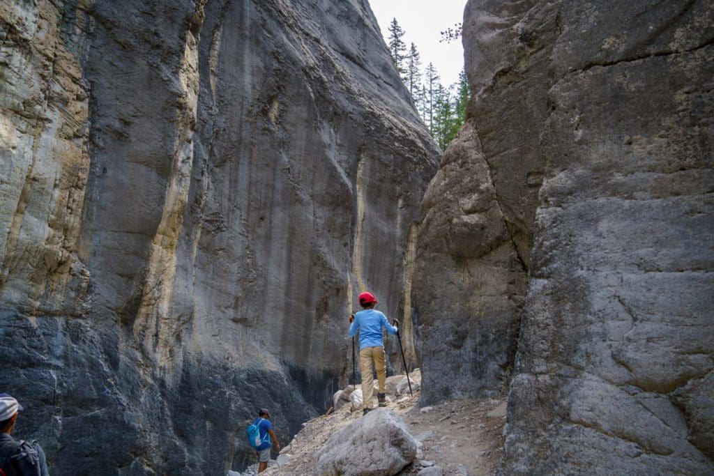 A young boy hikes through Grotto Canyon Trail, with large towering boulders on both sides near Canmore.