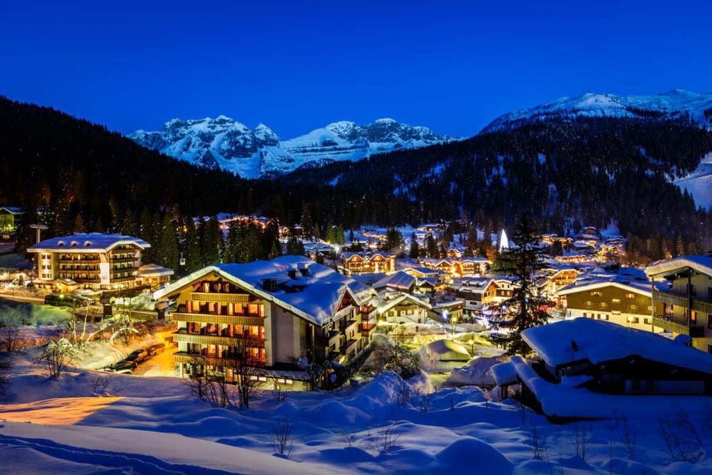 A view of Madonna di Campiglio, nestled in a mountain range in Italy, lit up at night.
