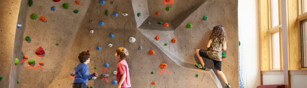 Several kids climb a rock wall while at Stowe Rocks Climbing Center, one of the best indoor things to do when skiing in Stowe with kids.