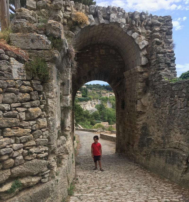 A young boy stands amongst stone walls in Roussillon, one of the best towns in the South of France with kids.