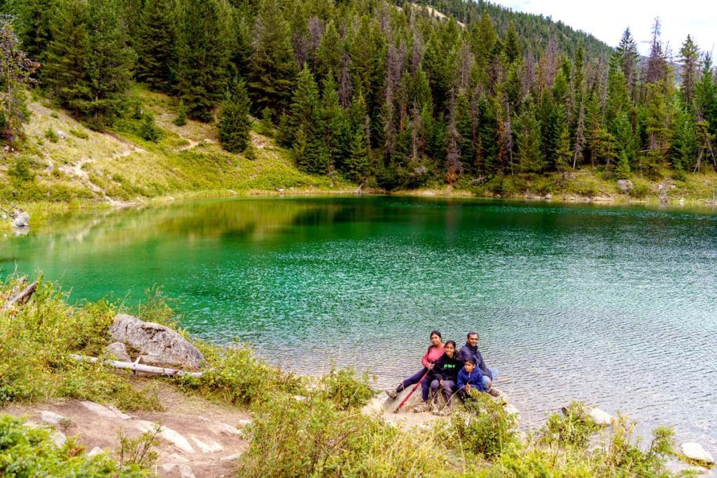 A family of four sits together on a large boulder on the shore of Valley of Five Lakes, while hiking near Jasper.