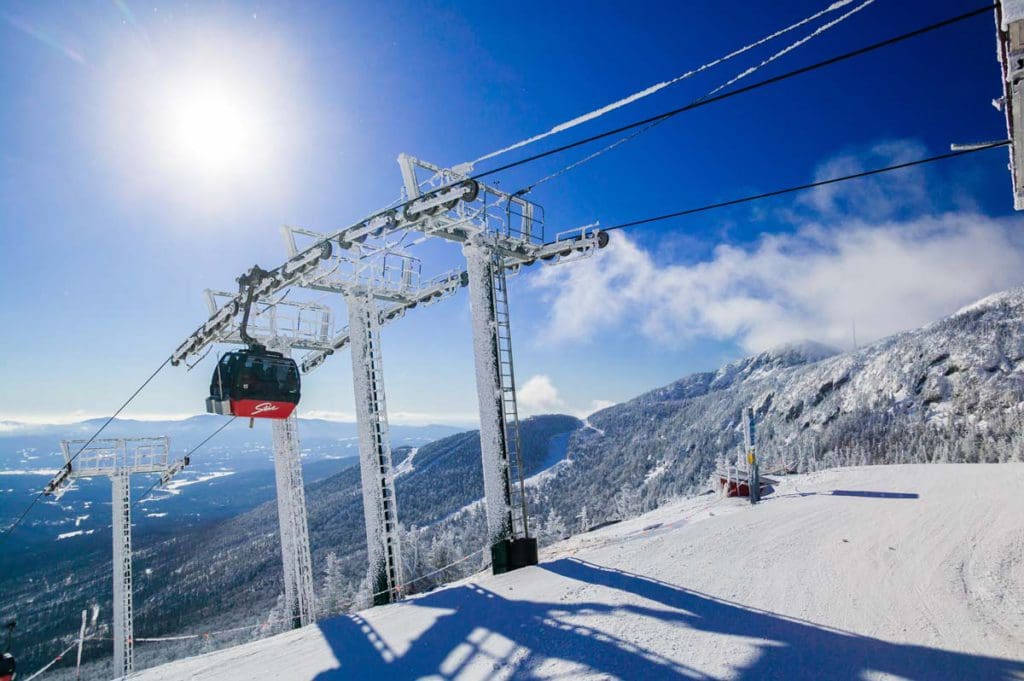 A gondola move along a track with snow on the ground on a scenic mountainside in Stowe, one of the best things to do when skiing in Stowe with kids.