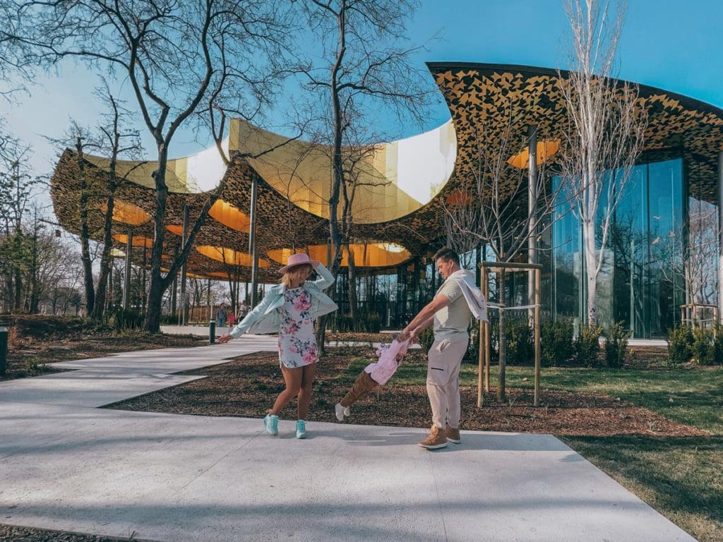 Two parents and their toddler daughter twirl in front of the House of Music.