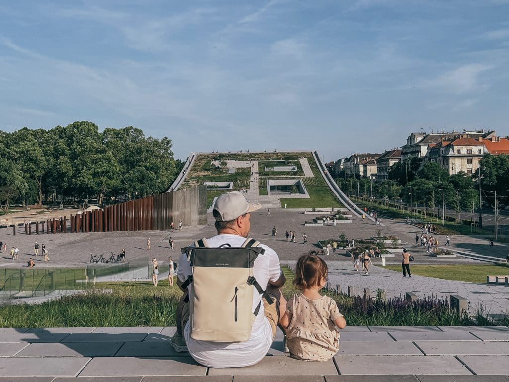 A dad and his young daughter sit near the Museum of Etnography and look out over City Park.