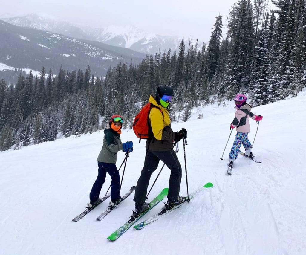 A dad and two kids pose on skis while enjoying the slopes in Big Sky, Montana.